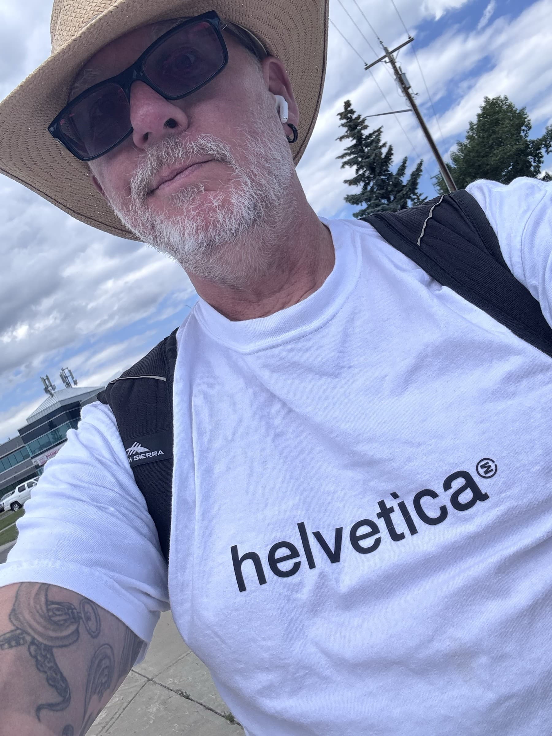 Michael Dargie wearing a Helvetica T-shirt and a wide hat, sunglasses, ferry in the background